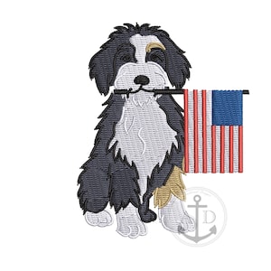 May include: Embroidered design of a dog holding a small American flag in its mouth. The dog has black, white, and tan fur. The flag has red and white stripes with a blue square and white stars in the corner. An anchor logo is in the bottom right.