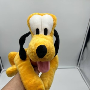 Puede incluir: Peluche de perro amarillo con orejas y nariz negras, ojos blancos y una lengua rosa que sobresale.