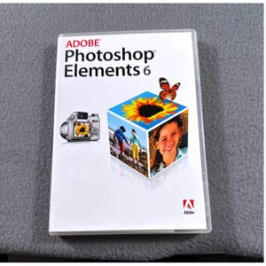 May include: Adobe Photoshop Elements 6 software box. The white box features the Adobe logo, product name, and a colorful graphic of a sunflower, a camera, a butterfly, and a smiling person. The software is in a clear plastic case.