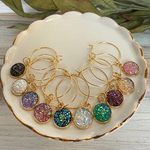 May include: Set of eight gold hoop wine glass charms with different colored glitter-filled round charms. The charms include black, white, purple, pink, teal, green, and two iridescent colors.