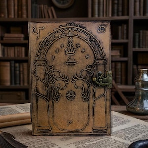 May include: A brown leather journal with an embossed design featuring an arched top with a crown, stars, and columns. The journal has a metal clasp and a detailed tree and floral pattern. The background shows a bookshelf.
