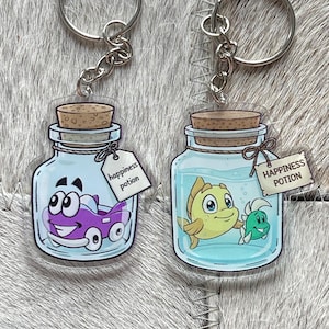 May include: Two acrylic keychains featuring clear glass jars with cork stoppers. One jar contains a purple cartoon car, the other a yellow and green fish. Both have a small white tag tied with string that reads "happiness potion" in black text.
