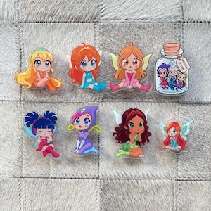 Op de afbeelding: Een verzameling van acht kleurrijke acryl bedels met een feeënthema. De bedels tonen cartoonfeeën in verschillende poses en outfits, met details zoals vleugels en accessoires. Eén bedel is een potje met het label "Happiness Potion."