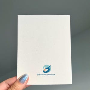Pu&ograve; includere: Un biglietto bianco con un'illustrazione blu e arancione di una padella con due uova. Il testo "@midnightsnacksca" &egrave; stampato sotto l'illustrazione.