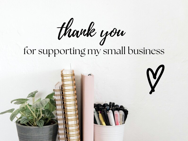 May include: A white wall with the text "thank you for supporting my small business" and a hand-drawn heart. There are three notebooks with gold spiral bindings and a pink notebook on a shelf. A potted plant and a cup of pens are also on the shelf.