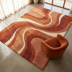 May include: A large, rectangular rug with a wavy pattern in shades of orange, cream, and brown. A matching orange armchair sits beside the rug. The rug's design creates a retro, textured look, suitable for a living room or bedroom.
