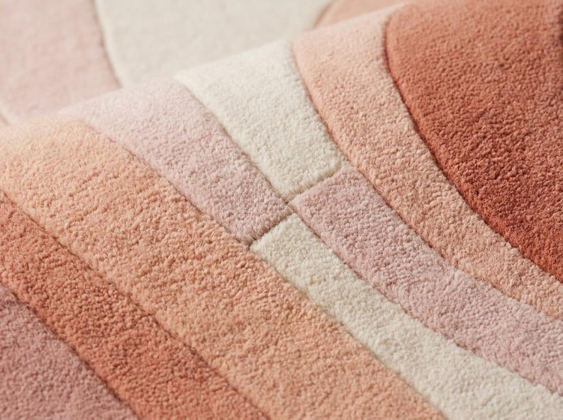 Puede incluir: Primer plano de una alfombra suave y texturizada con un dise&ntilde;o de arco&iacute;ris. La alfombra presenta rayas de diferentes tonos de rosa, melocot&oacute;n y crema. El material afelpado es visible, lo que sugiere comodidad y calidez. El dise&ntilde;o es moderno y acogedor.