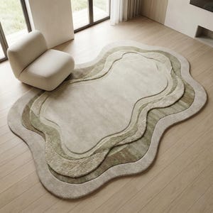 May include: A neutral-toned, layered area rug with an organic, flowing shape. The rug features varying shades of beige and green, creating a textured, dimensional effect. A cream-colored armchair sits nearby, complementing the rug's color palette.