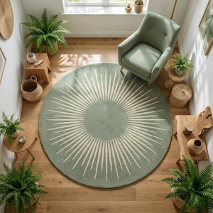 May include: A round, sage green rug with a sunburst design in cream. The rug is the focal point of a room with wooden floors, a green armchair, and small wooden tables with plants. The room is well-lit with natural light.