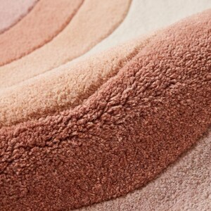 Close-up of hand tufted wool rug showing dense soft pile with carved abstract wave lines in blush pink peach and cream tones