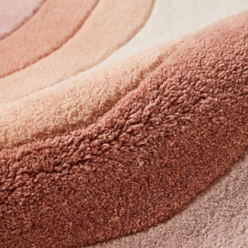 Close-up of hand tufted wool rug showing dense soft pile with carved abstract wave lines in blush pink peach and cream tones