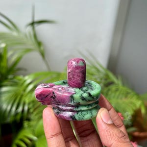 以下が含まれることがあります： 円筒形のトップと積層ベースを備えた、彫刻された宝石の彫刻。彫刻は主にルビーと緑色で、研磨仕上げです。オブジェクトは、緑の葉の背景に対して手で保持されています。