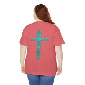 May include: Coral-colored t-shirt featuring a turquoise cross design on the back. The cross is composed of various seashells and aquatic elements. The shirt has short sleeves and a relaxed fit, suitable for casual wear.