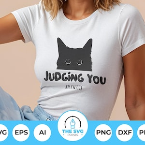Könnte beinhalten: Weißes T-Shirt mit einer schwarzen Katzen-Grafik und dem Text "JUDGING YOU SILENTLY". Das Design zeigt eine Katzenkopf-Silhouette mit Augen. Das Shirt ist ein kurzärmeliges Rundhals-Shirt.