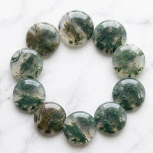 Peut inclure: Dix pierres rondes en agate mousse polies. Chaque pierre présente une base translucide avec des inclusions vertes et brunes complexes, évoquant des paysages miniatures. Les pierres sont disposées en cercle.
