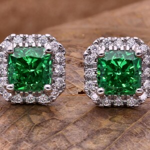 May include: A pair of emerald green square-shaped earrings with a halo of smaller diamonds around each stone.