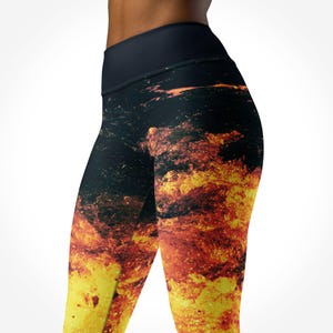Könnte beinhalten: Schwarze Leggings mit hohem Bund und feurigem Design. Die Leggings zeigen ein auffälliges Muster aus gelben, orangefarbenen und roten Farbtönen, das einen dynamischen visuellen Effekt erzeugt. Der Bund ist einfarbig schwarz.