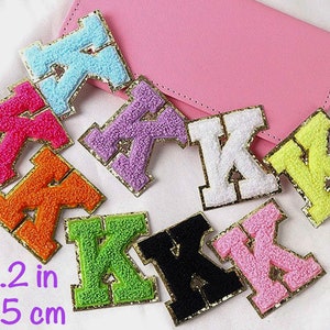 Könnte beinhalten: Sortiment von 10 flauschigen Buchstaben-K-Patches in verschiedenen Farben, darunter Pink, Lila, Orange, Grün, Gelb, Schwarz und Weiß. Jeder Patch ist 5,5 cm (2,2 Zoll) groß und hat einen goldenen Umriss.