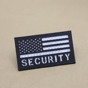 May include: Black and white embroidered patch with an American flag and the word "SECURITY" in white lettering.