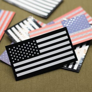 May include: A collection of rectangular stickers featuring the American flag design. The stickers have a black background with white stripes and stars. Some stickers have a holographic or metallic finish, and others have a red and blue color scheme.