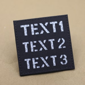 Könnte beinhalten: Schwarzer Patch mit weißem reflektierendem Text, der "TEXT 1", "TEXT 2" und "TEXT 3" lautet.