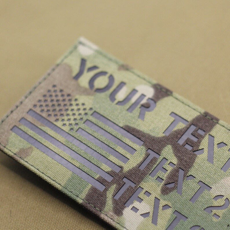 May include: A black and green camouflage fabric patch with a black American flag and the text "YOUR TEXT" repeated multiple times.