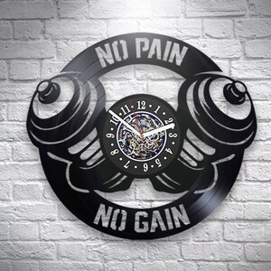 May include: Black vinyl record clock with a dumbbell design. The clock face features a black and white clock with Roman numerals. The clock is surrounded by the text "No Pain No Gain".