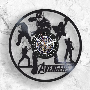 May include: Black vinyl record clock featuring the Avengers characters, including Captain America, Hulk, Thor, and Iron Man. The clock face is a circular design with Roman numerals and a black background. The clock is surrounded by a black frame with the word "Avengers" printed in white.