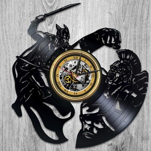 May include: A black vinyl record clock featuring a silhouette of two warriors in combat. The clock face is gold with Roman numerals and a detailed clock mechanism.