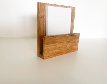 Könnte beinhalten: Ein Schreibtisch-Organizer aus Holz mit natürlichem Finish. Der Organizer hat eine vertikale Rückseite und eine untere, abgewinkelte Tasche. Ein Stapel weißes Papier befindet sich im Inneren. Die Holzmaserung ist sichtbar und verleiht Textur.