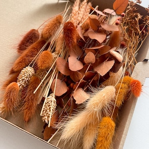 Könnte beinhalten: Eine Schachtel gefüllt mit getrockneten Blumen in Braun-, Orange- und Beigetönen. Die Blumen umfassen flauschige Hasenschwänze, Weizenhalme und Eukalyptusblätter.