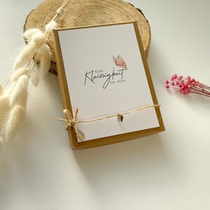 May include: A small gift box with a brown lid and a white card inside. The card has a butterfly illustration and the text "Eine Kleinigkeit f&uuml;r dich."  The box is tied with twine.