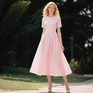 Peut inclure: Une robe midi rose clair à manches courtes, dotée d'un col rond et d'un corsage ajusté qui se prolonge par une jupe ample et plissée. Le tissu présente une texture subtile en forme de grille fine, offrant un aspect net et structuré.