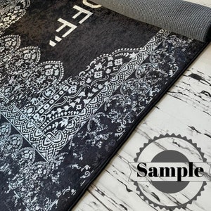 May include: Black and white area rug with a silver paisley pattern. The rug has the word "FREE" written in silver lettering on the top left corner.