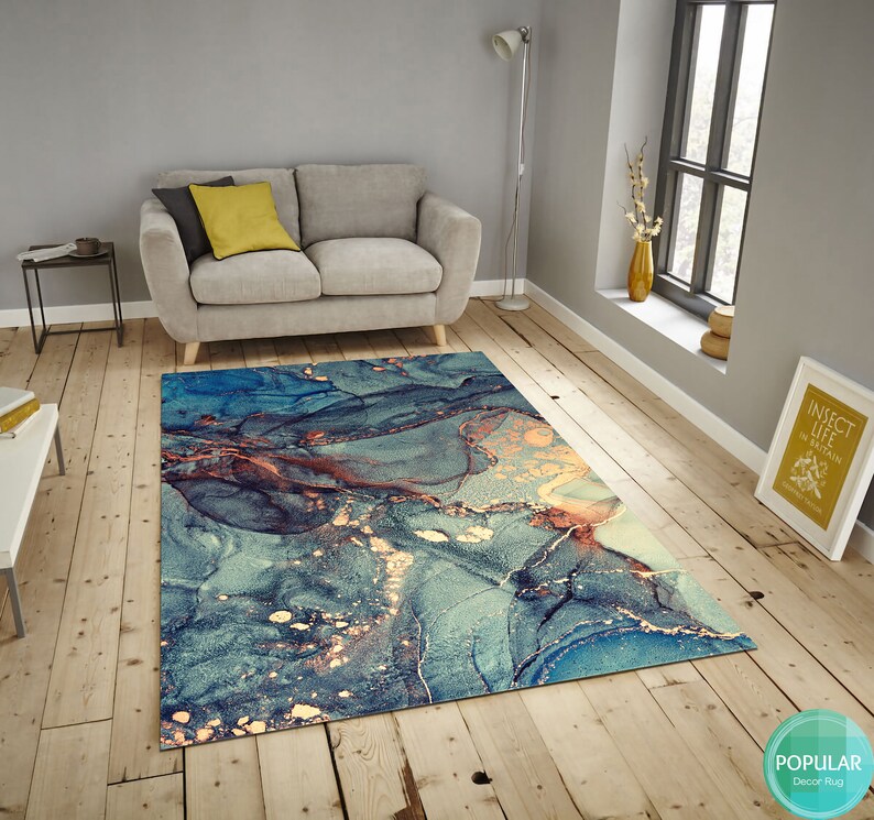 K&ouml;nnte beinhalten: Abstrakter Teppich mit einem blauen, goldenen und braunen Marmormuster. Der Teppich liegt auf einem Holzboden in einem Wohnzimmer.