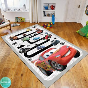 May include: A gray and white rug with a black race track design featuring cartoon cars, including Lightning McQueen. The rug is perfect for a child's room or play area.