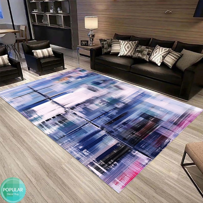 May include: Abstract area rug with a white background and blue, green, black, and pink brushstrokes. The rug is laid out on a wooden floor in a living room setting.