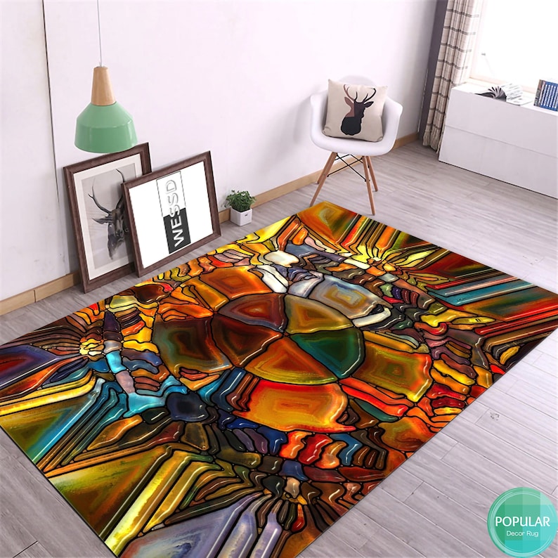 May include: Abstract stained glass style area rug with a colorful design of yellow, orange, red, blue, green, and brown. The rug has a geometric pattern with a central circular shape.
