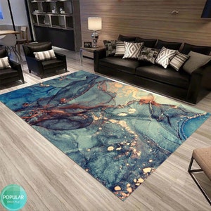 K&ouml;nnte beinhalten: Abstrakter Teppich mit einem blauen, t&uuml;rkisfarbenen und goldenen Marmormuster. Der Teppich liegt auf einem Holzboden in einem Wohnzimmer.