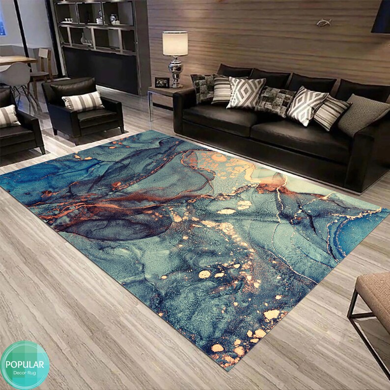 K&ouml;nnte beinhalten: Abstrakter Teppich mit einem blauen, t&uuml;rkisfarbenen und goldenen Marmormuster. Der Teppich liegt auf einem Holzboden in einem Wohnzimmer.