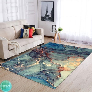K&ouml;nnte beinhalten: Abstrakter Teppich mit blauen, goldenen und braunen marmorartigen Mustern. Der Teppich liegt auf einem hellen Holzboden in einem Wohnzimmer.