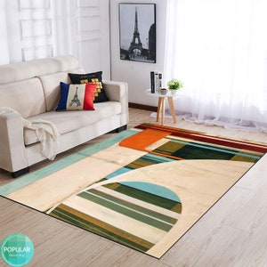 May include: Abstract geometric rug with orange, green, blue, and white stripes and shapes. The rug is on a light wood floor in a living room setting.