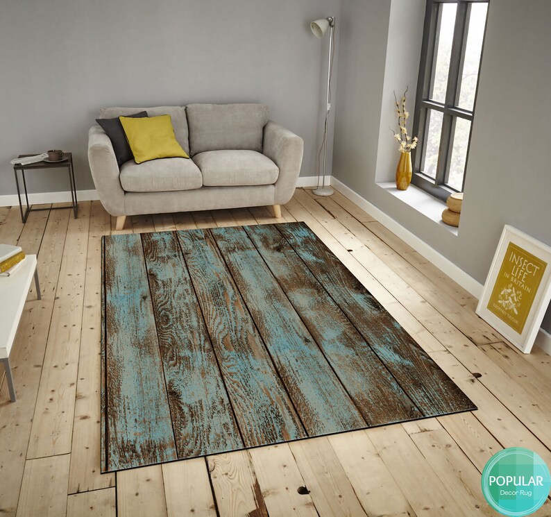 May include: A blue and brown distressed wood-look area rug with a rustic design. The rug is laid out on a hardwood floor in a living room setting.