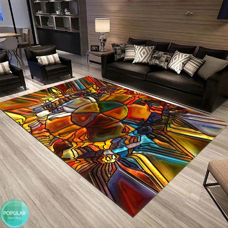 May include: Abstract stained glass style rug with a colorful design of red, orange, yellow, blue, green, and purple. The rug is laid out on a wooden floor in a living room setting.