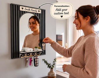 May include: A black wall-mounted mirror with vertical slats and a small shelf. The mirror features a light-colored wooden plaque at the top with the text "Smith Family" and two heart icons. Below the shelf are four metal hooks for hanging keys.