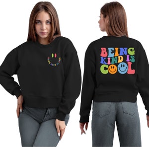 May include: Black cropped sweatshirt with the text "BEING KIND IS COOL" in rainbow colors with a smiley face on the back. The front of the sweatshirt has a small smiley face with the text "BEING KIND IS COOL" in a smaller font.