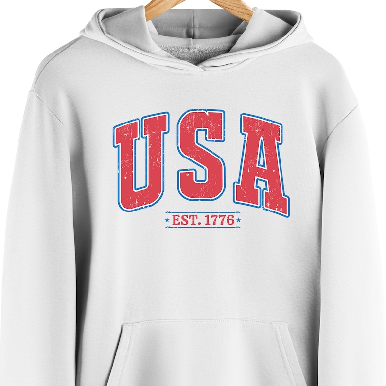 Op de afbeelding: Witte hoodie met een rode en blauwe vintage-stijl grafische afbeelding met de tekst "USA EST. 1776".