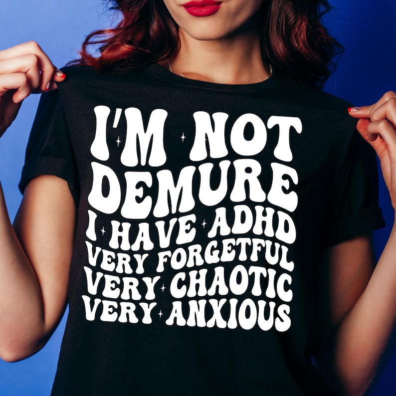 May include: Black t-shirt with white text that reads "I'm not demure I have ADHD very forgetful very chaotic very anxious".