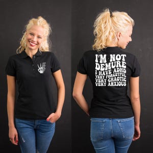 May include: Black polo shirt with white text that reads "I'm not demure I have ADHD very forgetful very chaotic very anxious".
