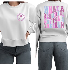 May include: White sweatshirt with a pink and blue smiley face on the front and the text "WHAT A BEAUTIFUL DAY FOR A TANTRUM" on the back.